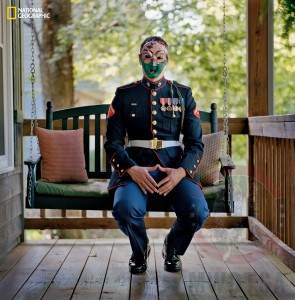 Marine Cpl. Chris McNair sitting on his parents' porch, in full uniform, wearing a mask he made in therapy.